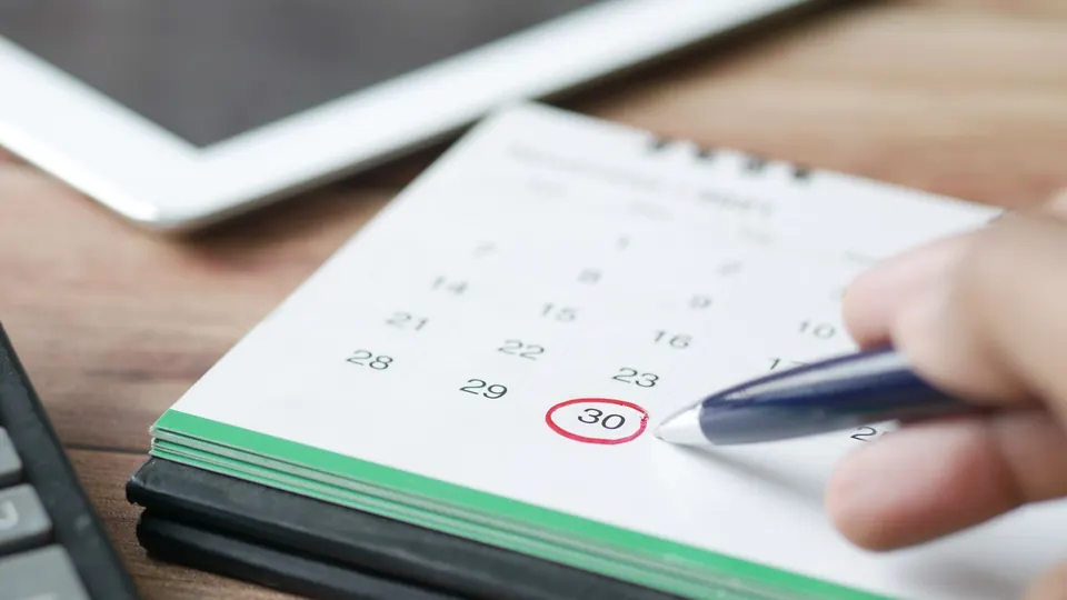 A hand circling a date on a desk calendar with a pen