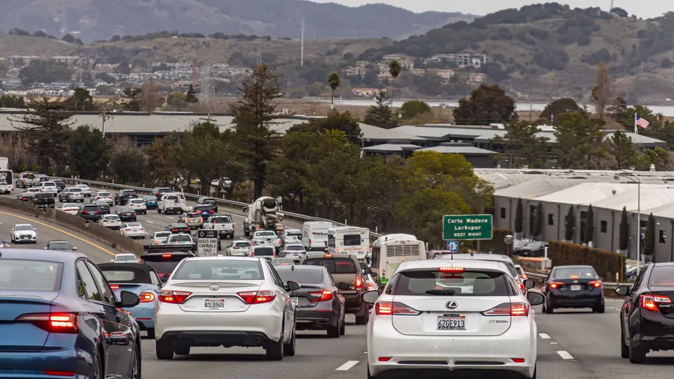 Cars driving in slow traffic on a California freeway with hills in the background