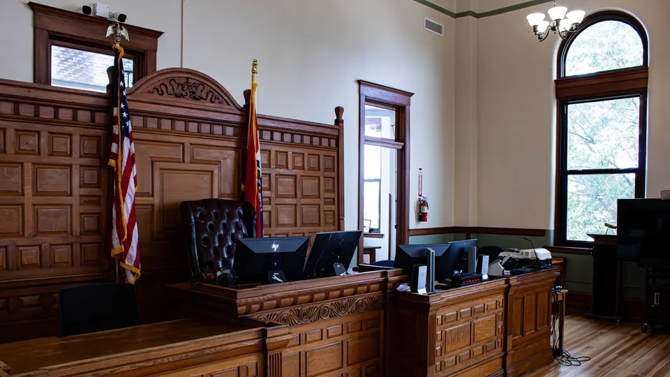An empty courtroom with a wood judge’s bench and American and state flags