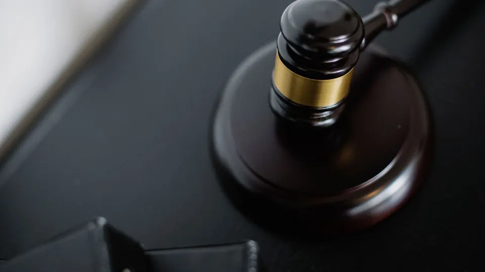 A wooden gavel with a brass band on its sound block on a dark desk