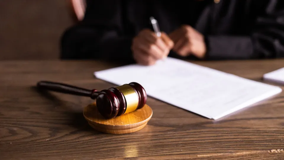 A gavel on a wooden desk beside a document being signed