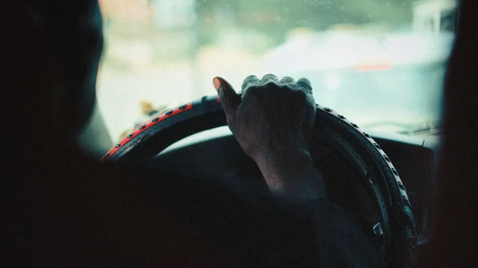 A driver’s hand resting on a steering wheel in a dark car cabin