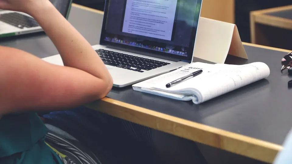 A laptop and a notebook on a desk, a person studying an online course