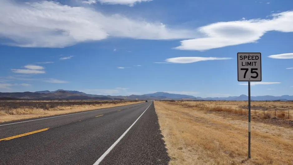 A two-lane highway running through open land with a speed limit 75 sign on the right shoulder