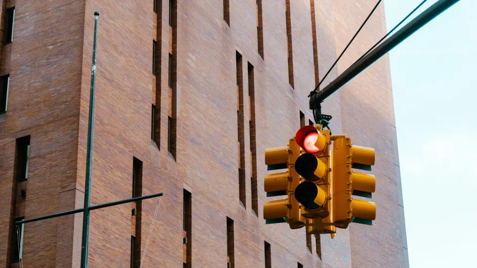 A traffic signal showing red, mounted on a pole beside a brick building in a US city