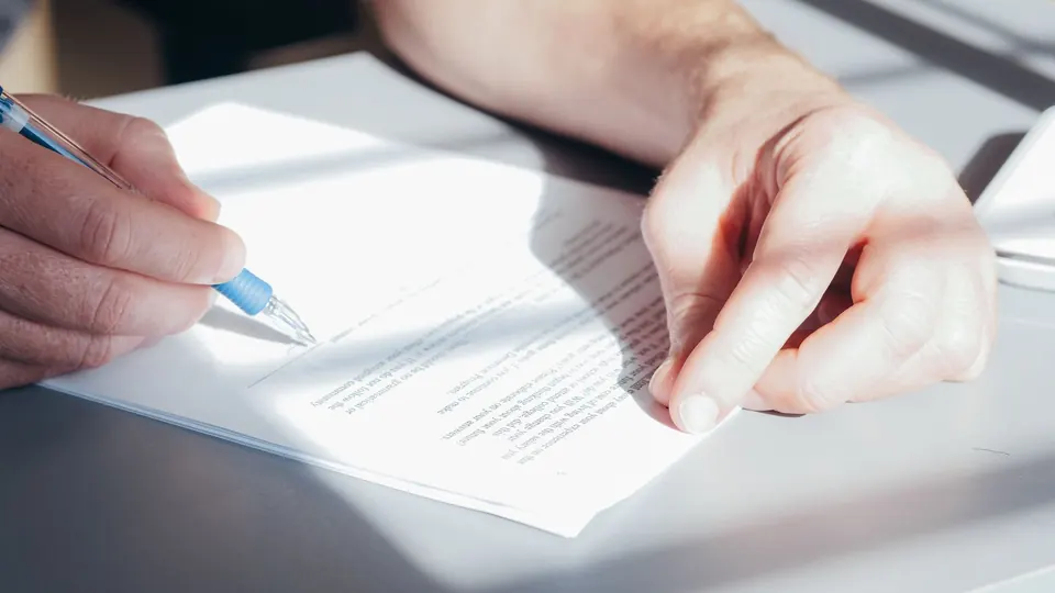 A hand holding a pen over a printed document, signing a written statement