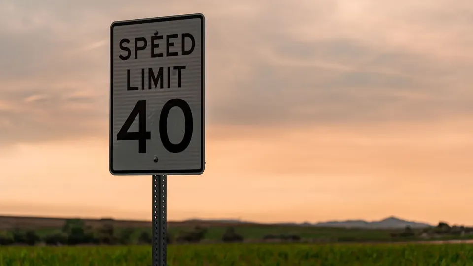 A black and white speed limit 40 sign on a post against an orange evening sky