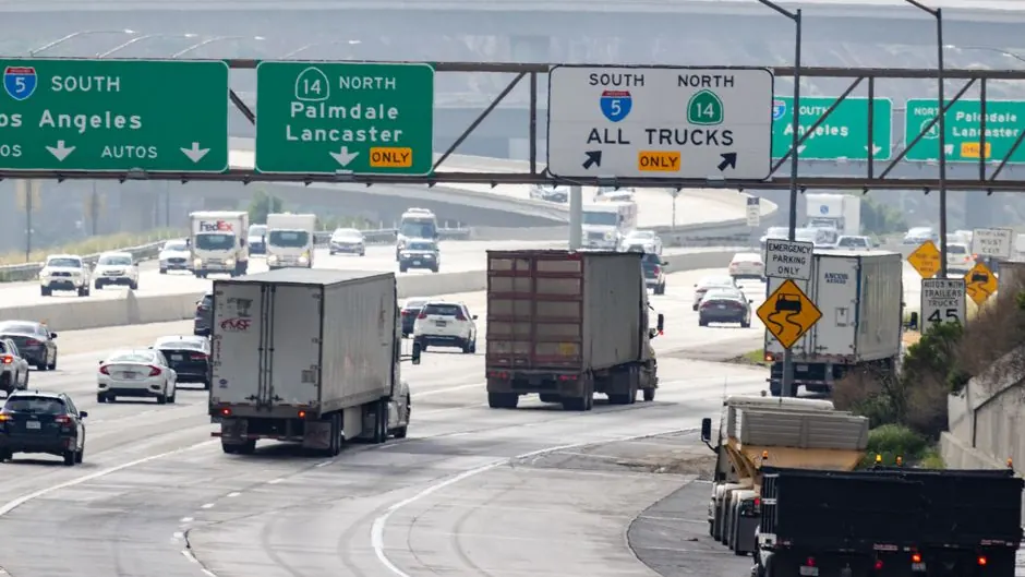 Semi trucks and cars on a Southern California freeway under signs for I-5 and all-trucks lanes